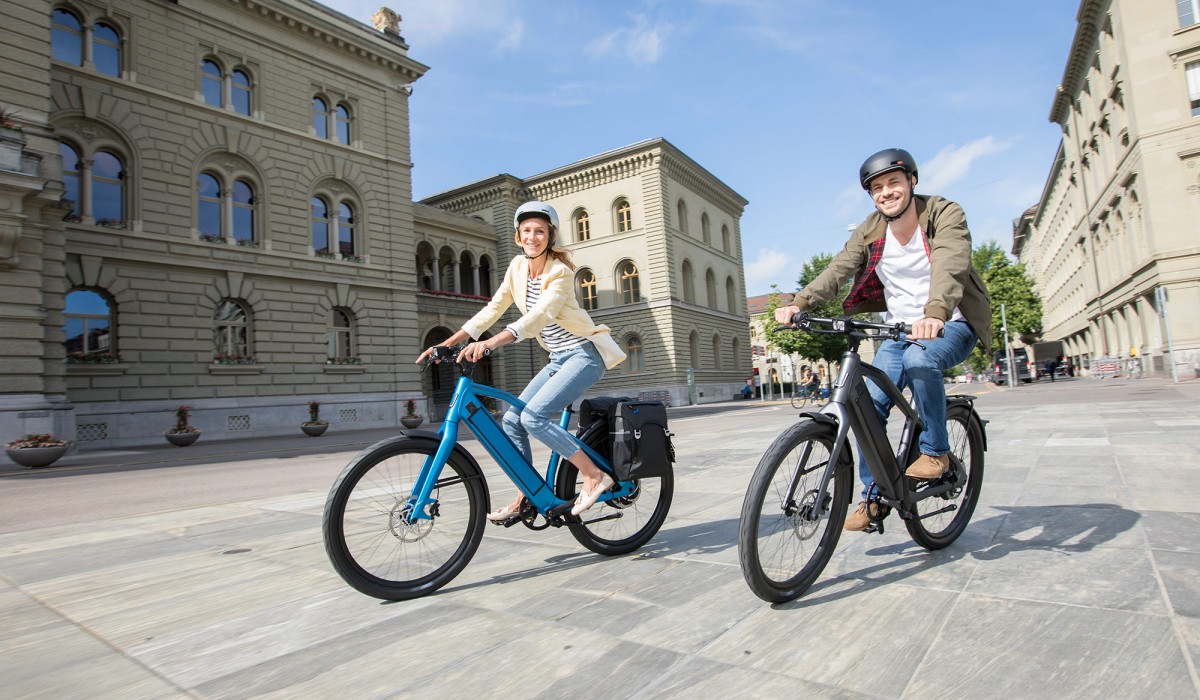 Paar mit Stromer ST2 E-Bikes in Royal Blue und Dark Grey bei Fahrt durch die Stadt.